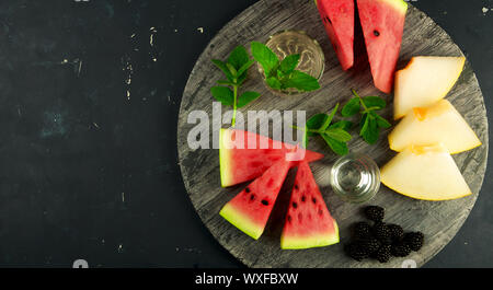 MELON WATERMELON BLACKBERRY AND MINT ON THE BACKGROUND. THREE PIECES OF RIPE WATERMELON JUICY MELON WITH RIPE BLACKBERRIES MINT Stock Photo