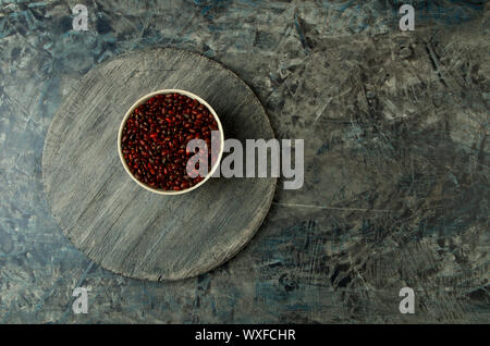 TEXTURE RELIEF SURFACE WITH A PLATE OF RED BEANS. UNEVEN BACKGROUND WITH WOODEN BOARD RAW RED BEANS IN THE DISH. Stock Photo