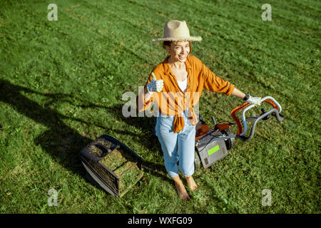 Portrait of a beautiful young woman dressed casually resting while cutting grass with lawn mower on the backyard Stock Photo