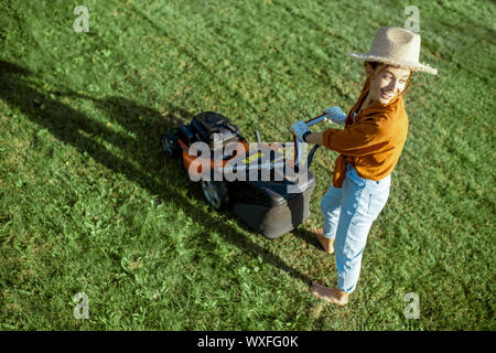 Portrait of a beautiful young woman dressed casually resting while cutting grass with lawn mower on the backyard Stock Photo