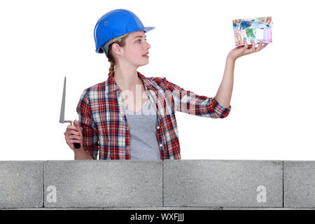 Female construction worker with a house made of money Stock Photo