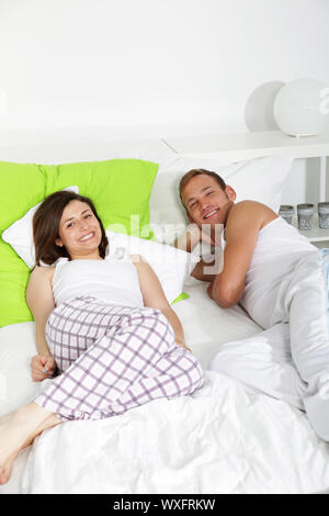 Young couple having a lazy day in bed smiling at the camera with copyspace Stock Photo