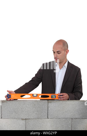 Man in a suit with a spirit level on a wall Stock Photo