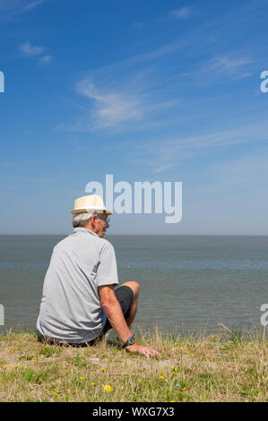 Elderly man is sitting on Dutch dyke in Lauwersoog Stock Photo