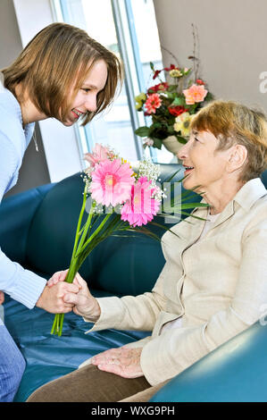 Granddaughter bringing colorful flowers to her grandmother Stock Photo