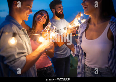 Happy friends with drinks toasting at rooftop party at night Stock Photo