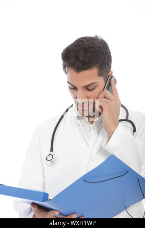 Young male doctor standing talking on a mobile phone while holding an open folder reading a patients medical history isolated on white Stock Photo