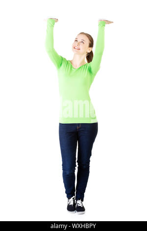 Smiling young woman is holding something abstract above her head. Happy girl with raised hands. Isolated on white background. Stock Photo