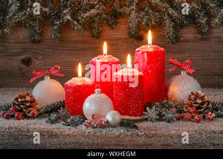 Natural Christmas decoration. Four red burning candles with christmas baubles and cones. Switzerland Stock Photo
