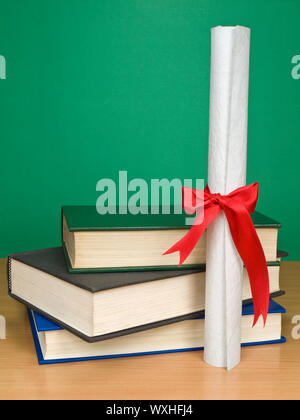 A pile of books and a diploma. Blank chalkboard on the background. Stock Photo