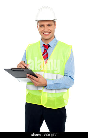 Smiling young construction engineer with safety hat writing on notepad against white background Stock Photo