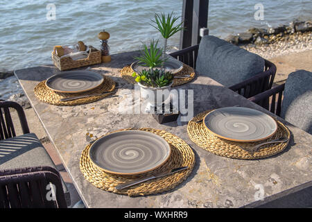 Beautiful served table of a modern cafe by the sea with dishes and flowers. Stylish restaurant for dinner on vacation Stock Photo