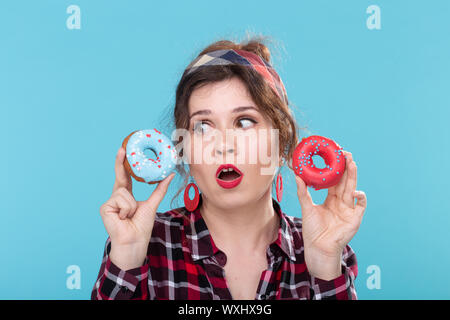 Junk food, diet and unhealthy lifestyle concept - pin-up woman with doughnuts over the blue background Stock Photo