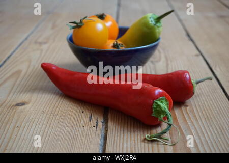 Set of multicolored sweet peppers and yellow heirloom tomatoes in a blue ceramic bowl on a rustic wooden table Stock Photo