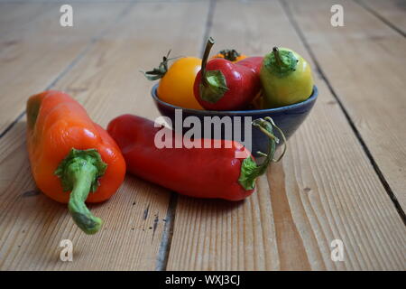 Set of multicolored sweet peppers and yellow heirloom tomatoes in a blue ceramic bowl on a rustic wooden table Stock Photo