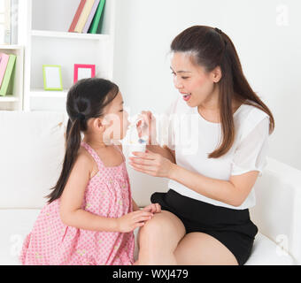 Eating yogurt. Happy Asian family eating yoghurt at home. Beautiful mother  feeding child, healthcare concept. Stock Photo