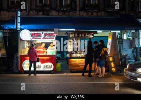 Taichung, Taiwan: Street food vendors selling food at the side of a street with customers waiting for their food an night Stock Photo