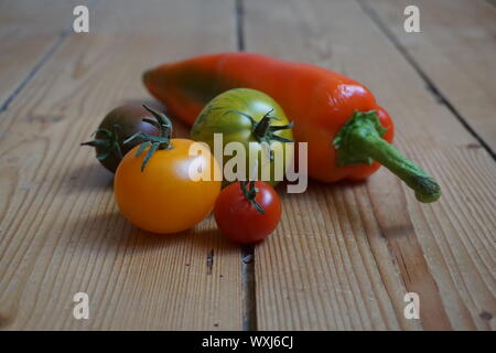 Set of multicolored long peppers and heirloom tomatoes on a rustic wooden table Stock Photo