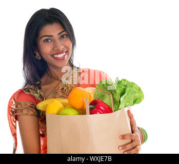 Happy grocery shopper. Portrait of beautiful traditional Indian woman in sari dress holding paper shopping bag full of groceries isolated on white. Stock Photo