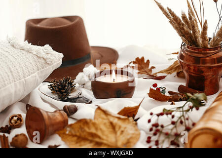 Hygge lifestyle. Candle, berries, fall leaves, herbs, acorns, nuts and brown hat on white fabric. Autumn mood. Hello autumn, cozy inspirational image. Stock Photo