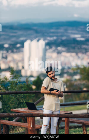 Young handsome minded man in jeans sitting at the table in nature and speaking on cellphone Stock Photo