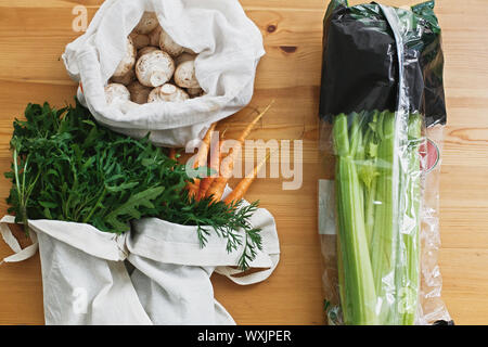 Ban plastic. Choose plastic free. Reusable eco friendly bag with fresh carrots,mushrooms,arugula and celery in cellophane plastic package on wooden ta Stock Photo