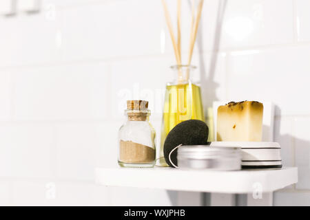 Eco natural shampoo, konjac sponge, fragrance oil, soap and ayurveda ubtan powder in glass on wooden shelf in bathroom, plastic free items. Sustainabl Stock Photo