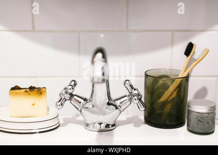 Eco natural bamboo toothbrushes, organic charcoal toothpaste in glass jar, soap bar on sink in bathroom. Zero waste bathroom concept. Plastic free ite Stock Photo