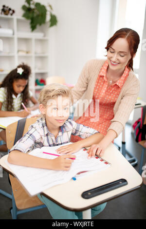 Blonde-haired schoolboy listening to teacher and noting down Stock Photo