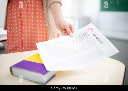 Teacher wearing spotted dress holding answer sheet for tests Stock Photo