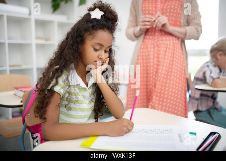 Cute dark-skinned girl holding pencil while writing test Stock Photo