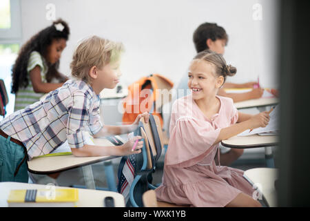 Cheerful girl wearing pink dress smiling while talking to classmate Stock Photo