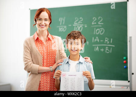 Red-haired teacher smiling and hugging her clever pupil Stock Photo