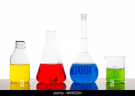 Four measuring glasses on a table of a chemical laboratory with red, yellow, blue and green liquid on white background Stock Photo