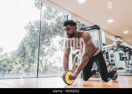 Athlete sporty man doing exercise with abs roller wheel to strengthen his abdominal muscle in gym. Stock Photo