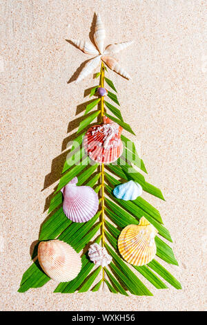 Christmas tree made of green palm thee brunch with different seashells as a decoration on sand, top view, vertical composition Stock Photo