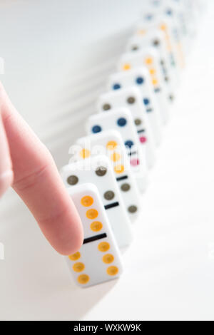 Finger about to knock over line of colourful dominoes on white background Stock Photo