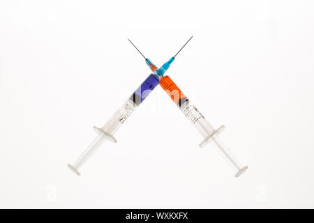 Two syringes holding purple and orange liquid crossing on white background Stock Photo