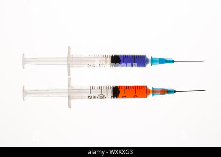 Two syringes holding purple and orange liquid beside each other on white background Stock Photo