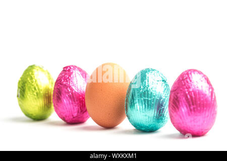 Four easter eggs in a row with one real egg on white background Stock Photo