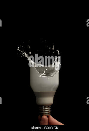 Hand holding light bulb turning to liquid against black background Stock Photo