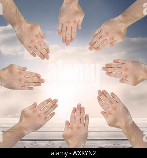 Group of hands forming a circle over blue sky and clouds in the background Stock Photo