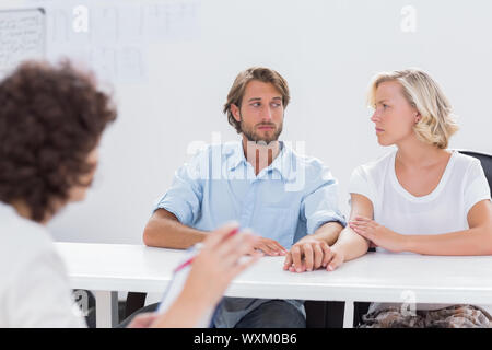 Couple looking doubtful during therapy session as therapist is gesturing at them Stock Photo