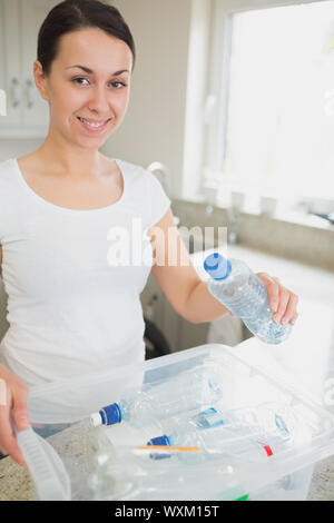 Woman throwing many bottles into recycling bin in kitchen Stock Photo