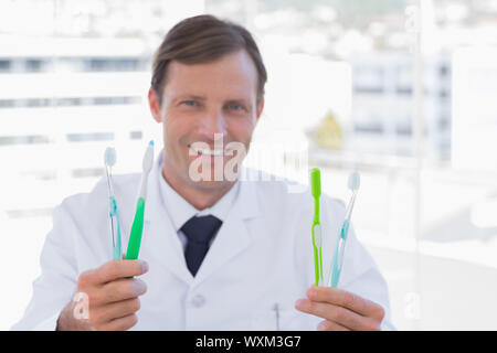 Smiling doctor holding two toothbrushes in his office Stock Photo