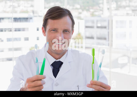 Happy doctor holding two toothbrushes in his office Stock Photo