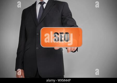 Businessman touching orange tag with the word seo written on it on grey background Stock Photo