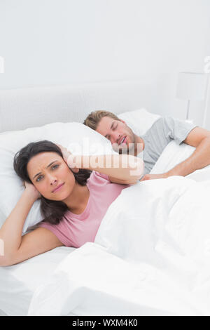 Woman covering her ears while her husband is snoring next to her Stock Photo