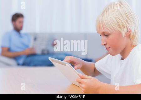 Boy using tablet while his father is reading on the couch Stock Photo