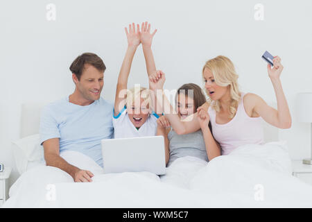 Family using a laptop in bed and raising their arms to show their success Stock Photo
